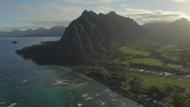 Aerial view of the Kualoa Ranch and Valley with the iconic mountain as seen above the turquoise pacific ocean during sunset