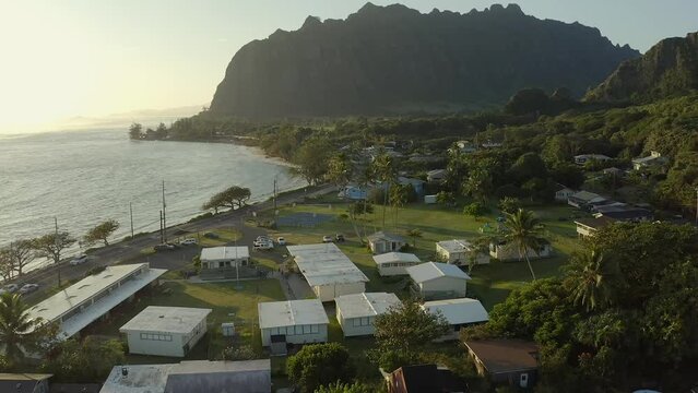 Aerial shot passing over an elementary school as kids are seen playing outdoors during sunrise in the town of Kaaawa Hawaii
