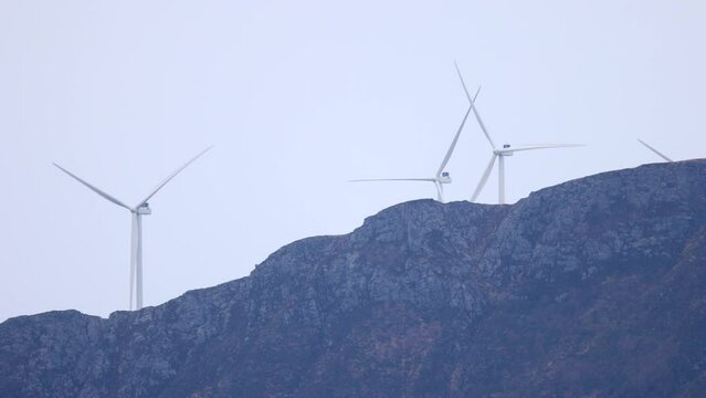 Wind turbines sticking up behind a mountain peak. The turbines are located on Harams&oslash;ya, north of &Aring;lesund city in Norway.