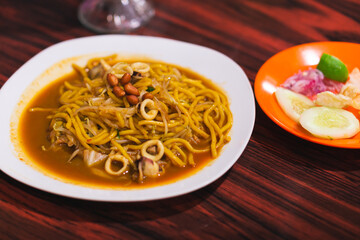 Mie Aceh is spicy noodle cuisine in Indonesia. Yellow noodles cooked with spices, herb, squid and has curry taste. Served with fried nut, shallot pickles. Focus selection and blurry selection.