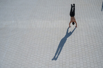 Shirtless man walks on his hands outdoors. View from above.