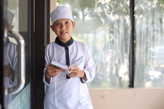 Smiling Asian muslim boy wearing muslim rob and skullcap with Quran. 