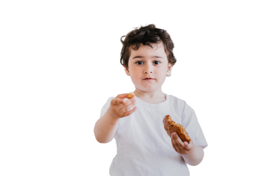 Little curly caucasian boy in white t-shirt at kitchen holding cookie in hand, offering a piece. Cute Italian kid, preschooler at breakfast, looks at camera against transparent background. Childhood