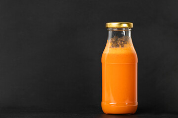 Freshly squeezed carrot juice in a glass bottle with golden cap on black textured background. Healthy living concept.