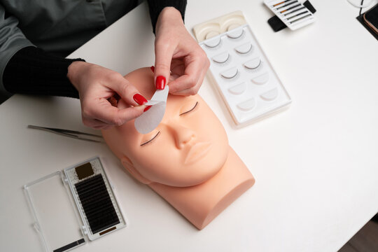 A beauty mannequin training head with a person practicing lash extension techniques. Female hands preparing glue cotton tape under eye. Basic training to build eyelashes.