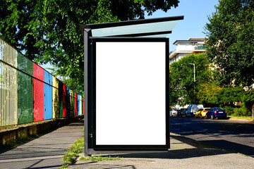 bus shelter at a busstop. blank billboard ad display. empty white lightbox sign. glass and aluminum frame structure. city transit station. urban street and green park setting. outdoor advertising.