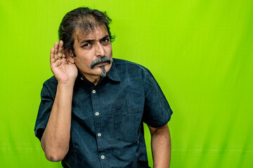 The well-dressed Indian man, dressed in a black shirt, stands against a green screen background and...