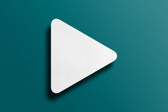 White paper cut into triangle shape, play button set on green paper background.