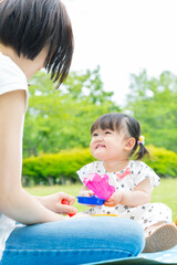 公園でお母さんを見つめ遊ぶ幼い女の子。育児イメージ