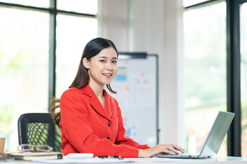 Portrait of pretty cheerful girl smiling while working on laptop in office