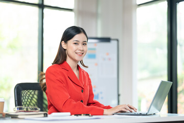Portrait of pretty cheerful girl smiling while working on laptop in office