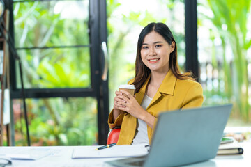 Young minded successful employee business woman in yellow shirt work hold takeaway delivery craft paper cup coffee sitting at desk with laptop pc computer at office indoor achievement career concept