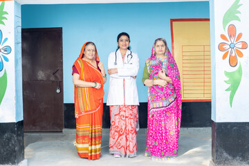Portrait of two Indian woman wearing sari or saree standing with female doctor are looking at camera, Rural healthcare and medical concept.