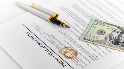 two wedding rings against the background of a marriage agreement, a fountain pen and dollar bills	
