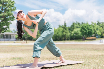 公園でヨガマットを使ってヨガ・ストレッチ・運動をする女性(プレイヤーズツイストのポーズ)
