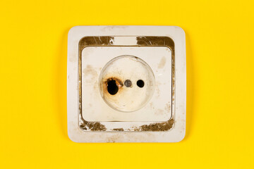 An old burned-out electrical outlet. Dirty socket on a yellow background.
