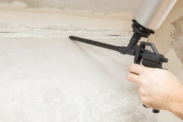 Young adult man hand holding and using professional foam spray gun and filling channel with new...
