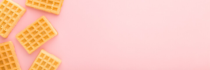 Fresh golden waffles on light pink table background. Pastel color. Wide banner. Closeup. Sweet snacks. Empty place for text. Top down view.