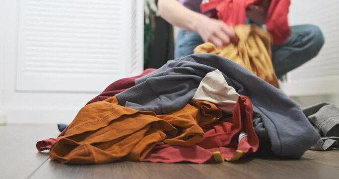 Woman collects dirty clothes lying in pile on floor in room. Bottom angle. Concept of homework, cleaning, putting things in order, washing clothes, sorting, charity.