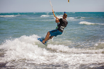 Professional kiter does the difficult trick. A male kiter rides against a beautiful background of waves and performs all sorts of maneuvers.
