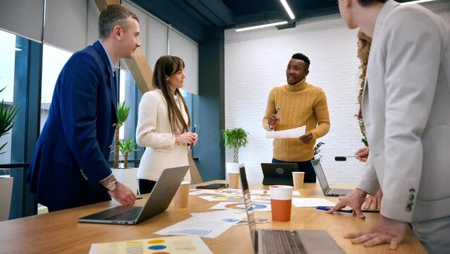 Black male team leader at business meeting in an office, discussing business affairs with other workers, papers and gadgets on the table