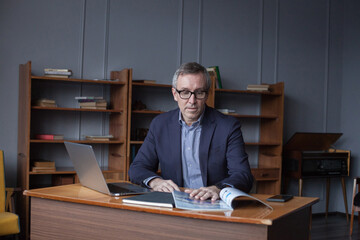 Portrait of mature serious businessman in suit and glasses reading book  in office