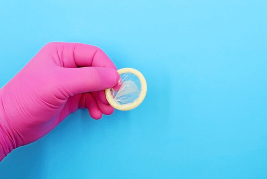 Hand with pink glove showing a condom, on blue background. Concept of prevention of sexually transmitted diseases or pregnancy