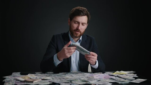 A man in a suit counting a money in his hand and smelling it before dropping it. He looks focused. The man is in black room. High quality 4k footage 