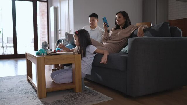 Concentrated Asian family spending time together doing their things on the couch