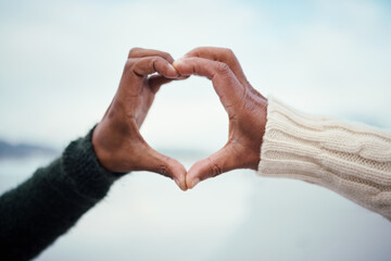 Black couple, heart hands and love by the sea with support and care outdoor. Blurred background, beach and ocean adventure date of people together with romantic emoji hand sign in nature on holiday