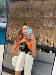 Woman in orange top and cosy comfy pants at home outdoor take photo selfie on phone with puppy miniature schnauzer in mirror for social media, stories, vertical