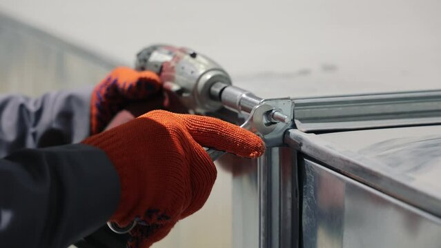 The craftsman tightens the bolt and nut with an electric screwdriver.