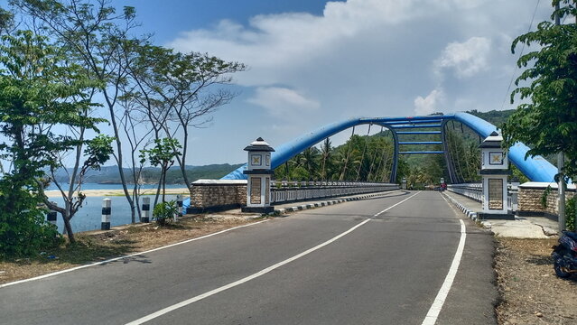 Road to the sea with blue arch bridge and blue sky in Pacitan, Indonesia.