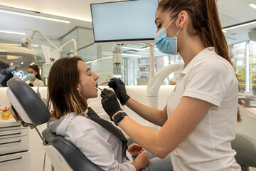 woman dentist in special uniform examines the teeth of a young girl patient in a dental chair.