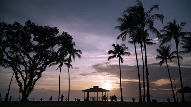 Tanjung Aru Beach - Silhouetted Tropical Palms and People Tourists Walking Against Dramatic Sunset Sky by the Sea at Shangri-la Resort Kota Kinabalu, Sabah, Malaysia - static wide angle