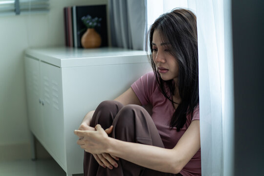 Asian young upset depressed woman sitting alone in living room at home.