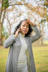 Confused 60s aged Asian woman on the phone, getting lost with her grandchild in the park.