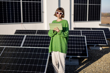Young woman with a digital tablet monitors energy production from the solar power plant on rooftop of her household. Concept of new technologies in alternative energy
