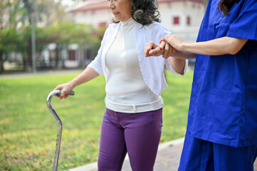 Cropped image of a caring female caregiver is helping an old lady walk with a walking stick