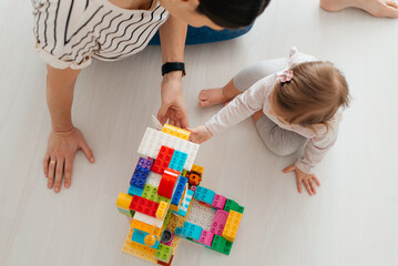 young nanny and adorable child playing with multicolored building blocks on floor