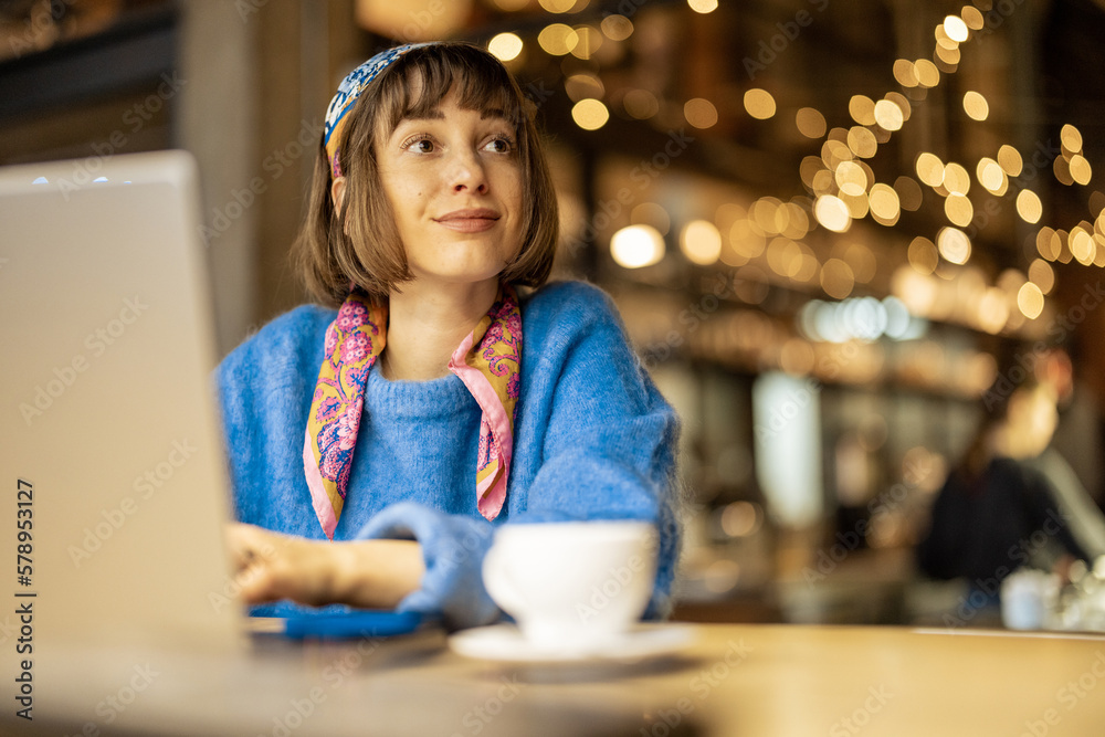 Wall mural young stylish woman works on laptop while sitting with a coffee drink at modern cafe. concept of rem