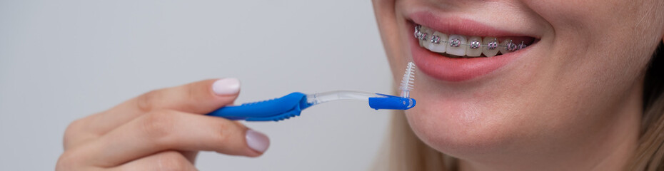 Caucasian woman cleaning her teeth with braces using a brush. Widescreen. 