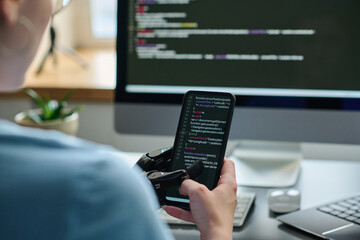 Close-up of IT specialist working with codes on smartphone connecting it with computer and...