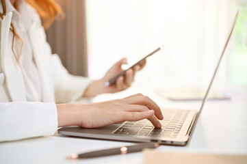 Side view image of professional millennial Asian businesswoman using her phone and laptop