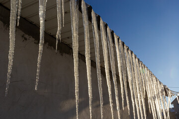 Icicles hang on the roof of a house against a bright blue sky. Spring landscape with icicles...