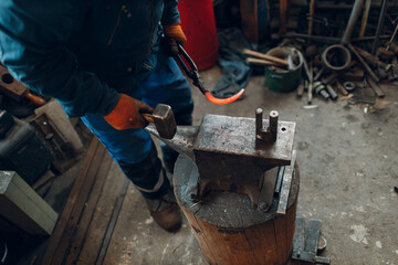 Blacksmith forges and makes metal horseshoe with hammer and anvil at forge.
