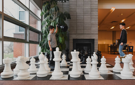 Two young boys playing chess with giant pieces in library