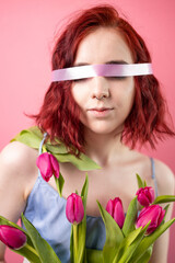 Beautiful blindfolded woman with bouquet of tulips flowers closeup portrait on pink background