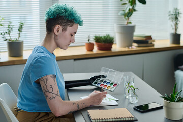 Young girl with prosthetic arm sitting at table and painting picture with paints