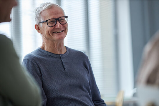 Portrait of smiling senior man laughing while chatting with friends in retirement home, copy space
